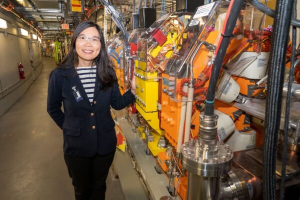 Guimei Wang standing next to the powerful magnets in the NSLS-II storage ring that steer, stabilize, and store electrons racing around at near light speed. (David Rahner/Brookhaven National Laboratory)